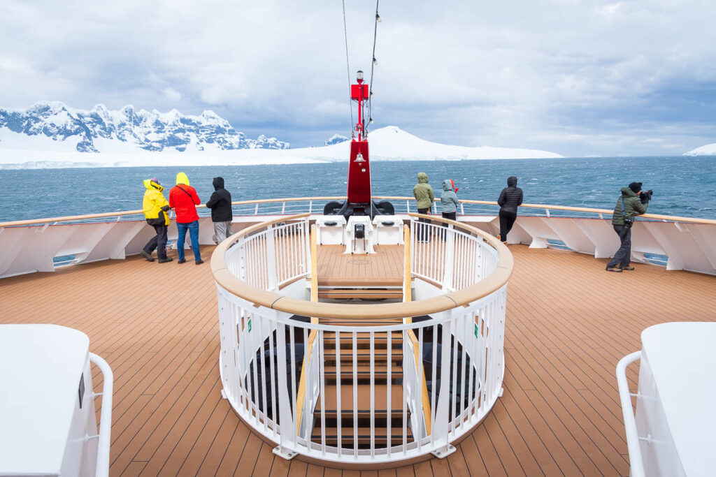 People on the deck of a ship in Antarctica with mountains in the background.
