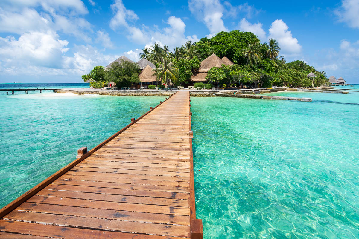 Wooden bridge leading to island in Maldives surrounded by turquoise waters.