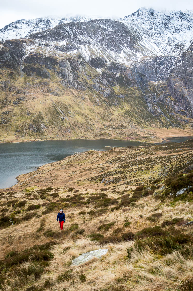 Woman walking up a hill with mountains and lakes down the hill behind.