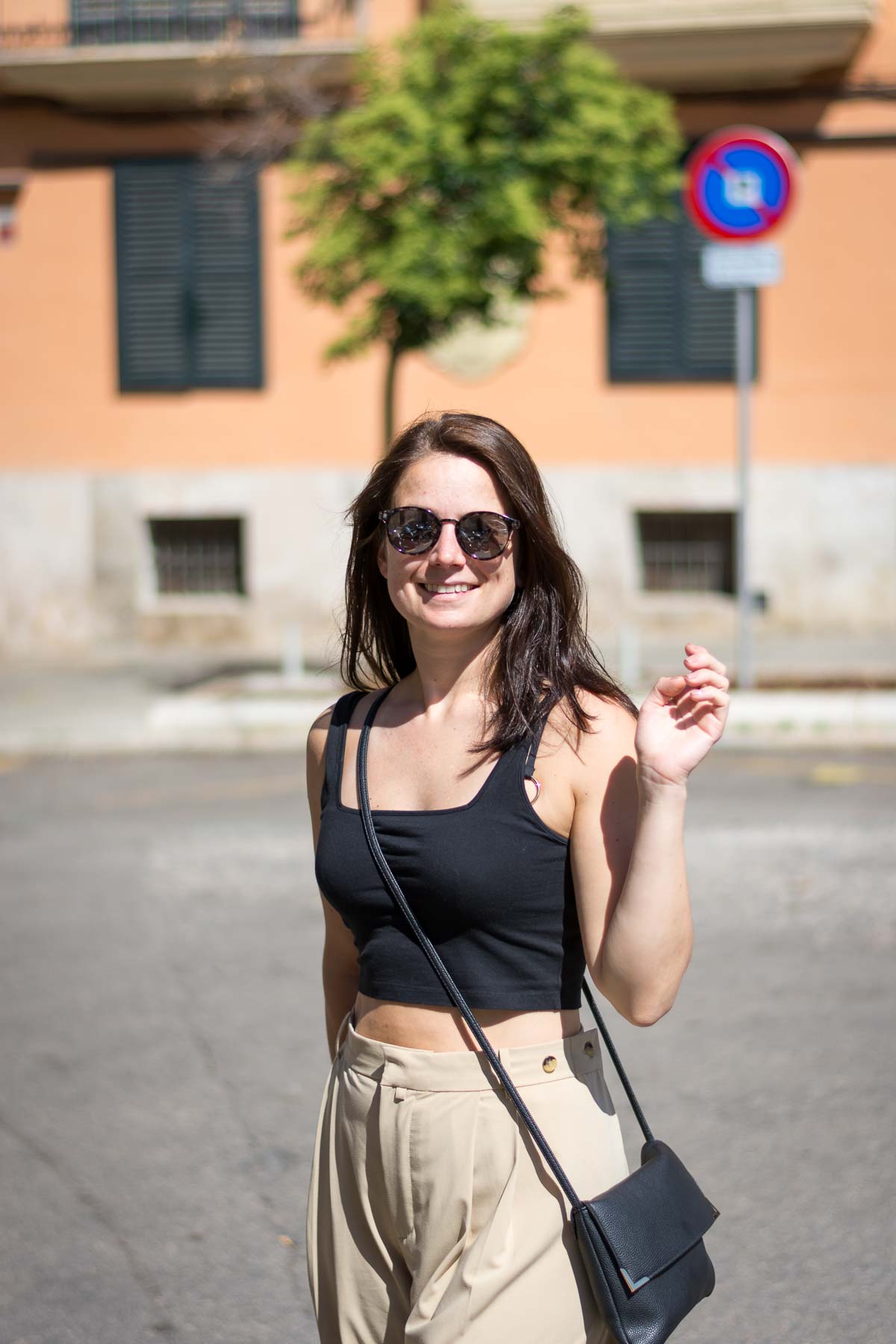 A woman in black crop top and beige trousers in a square in palma de mallorca. 