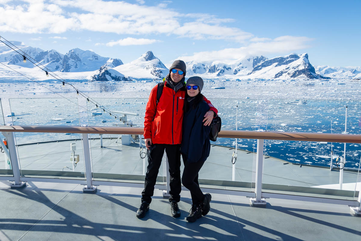 Seb and ieva standing on deck with the yalour islands in the background surrounded by sea ice and icebergs.