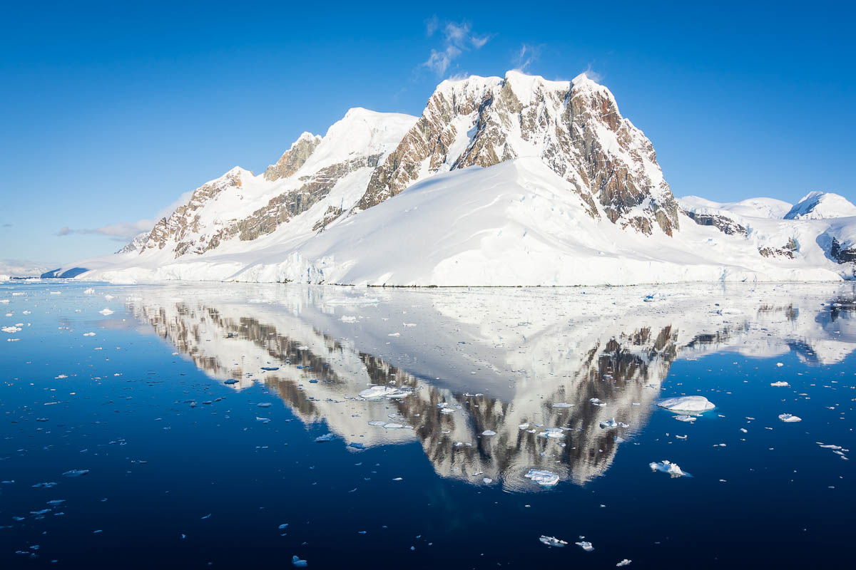 Snow-covered mountain at the entrance to the Lemaire channel, with a reflection on the calm water.