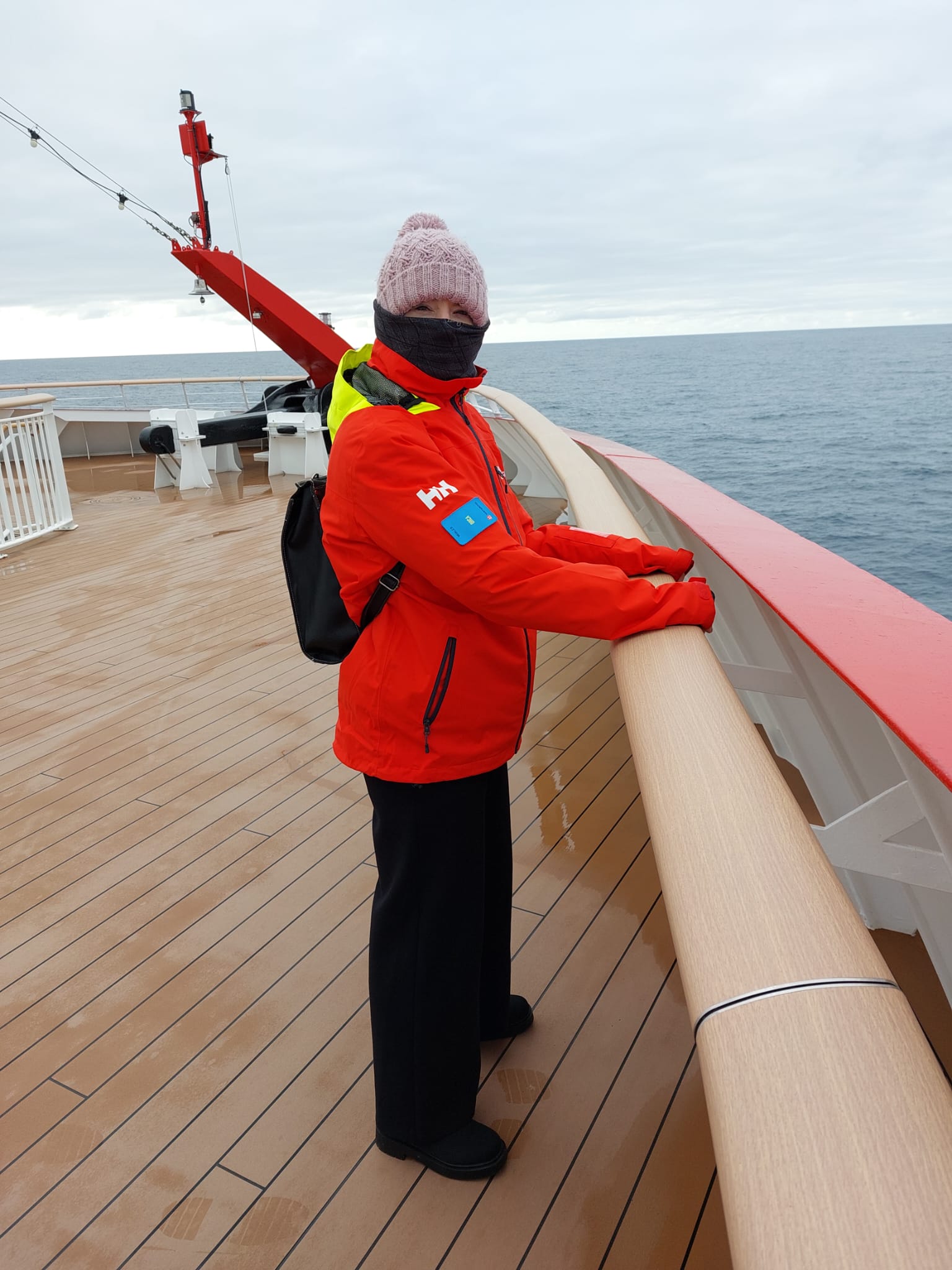 A woman dressed in warm clothes and red windproof jacket on deck of an Antractic Cruise ship.