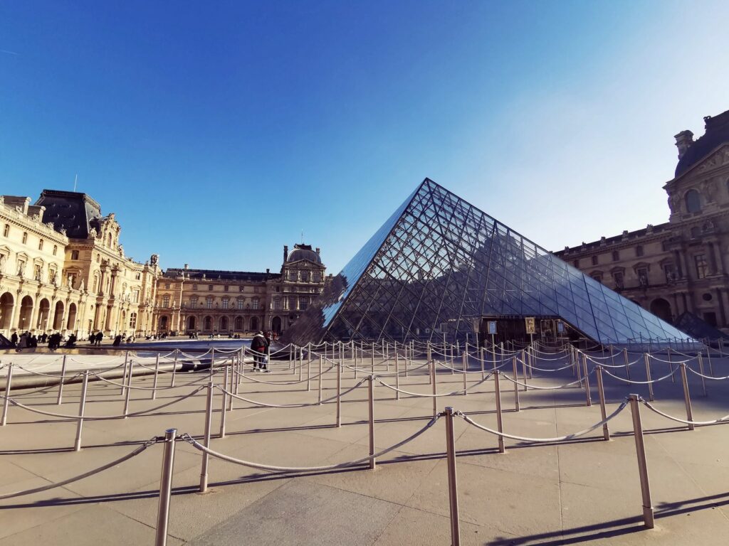 Louvre Pyramid in Paris with bright sky, showcasing iconic architecture and clear reflections.