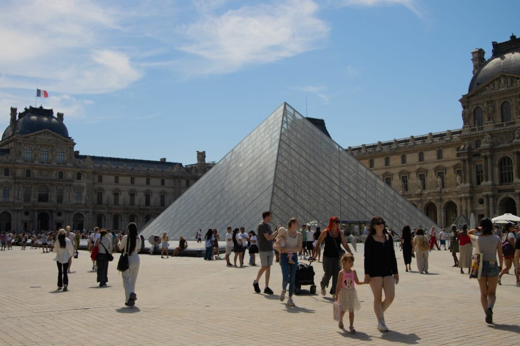Visitors enjoy a sunny day at the iconic Louvre Pyramid in Paris, France.