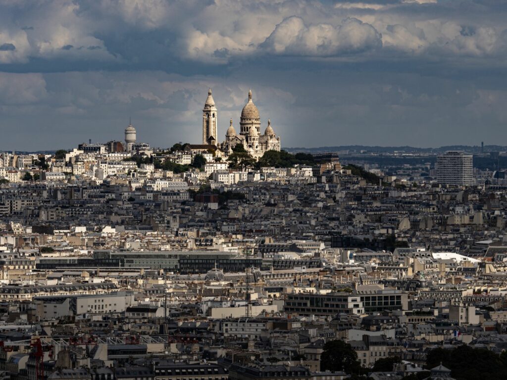 A striking view of the Sacré-Cœur Basilica amidst the Paris skyline with dramatic clouds above.