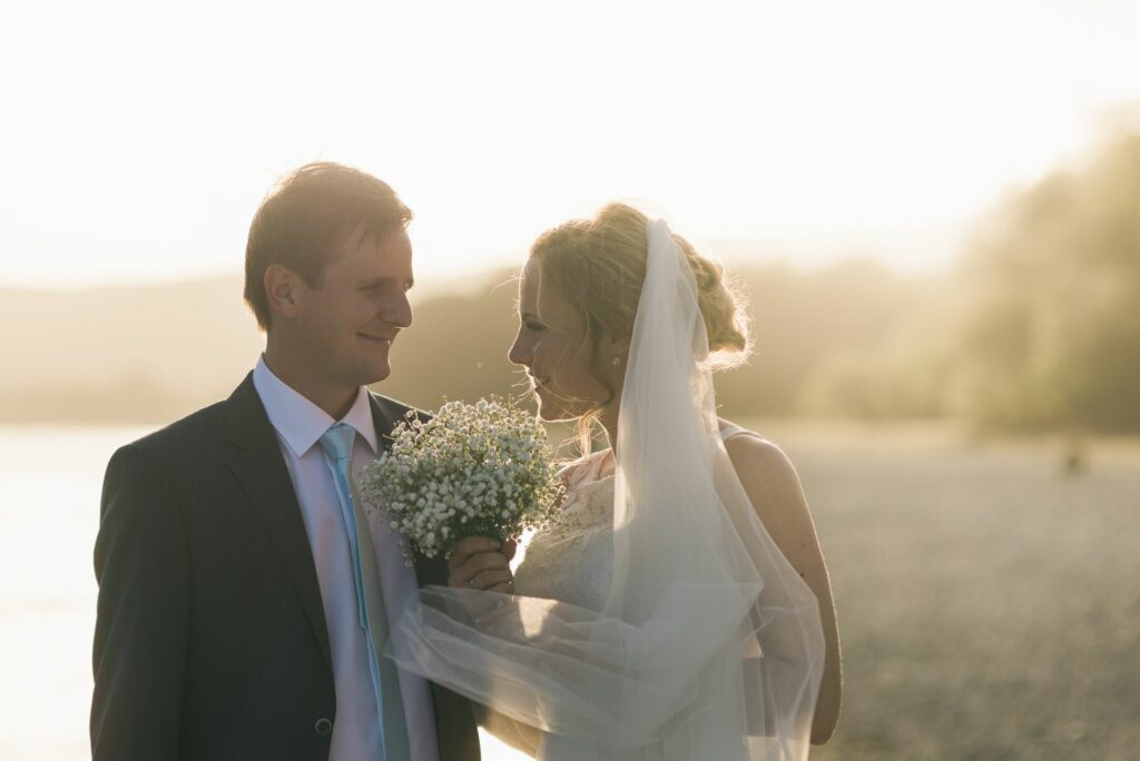 Bride and groom share a tender moment at sunset on a serene beach, creating a romantic wedding scene.