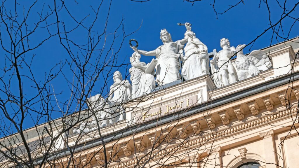 Elegant statues adorning a historic building facade under a clear blue sky in Vienna, Austria.