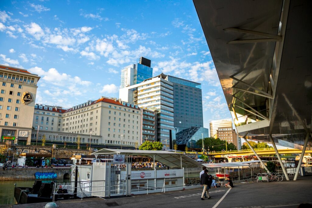 Urban scene in Vienna with modern architecture and a canal, showcasing bustling city life.