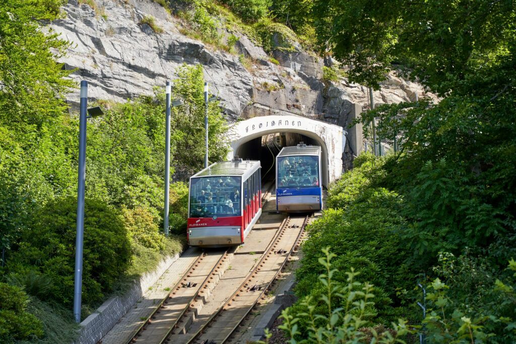 A vibrant view of the Fløibanen funicular entering a rocky tunnel surrounded by greenery.