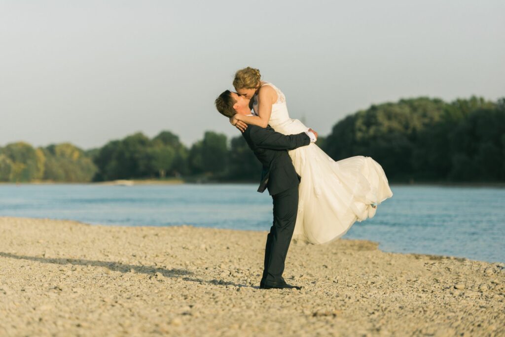 Bride and groom embracing joyfully on a scenic beach, celebrating their wedding.