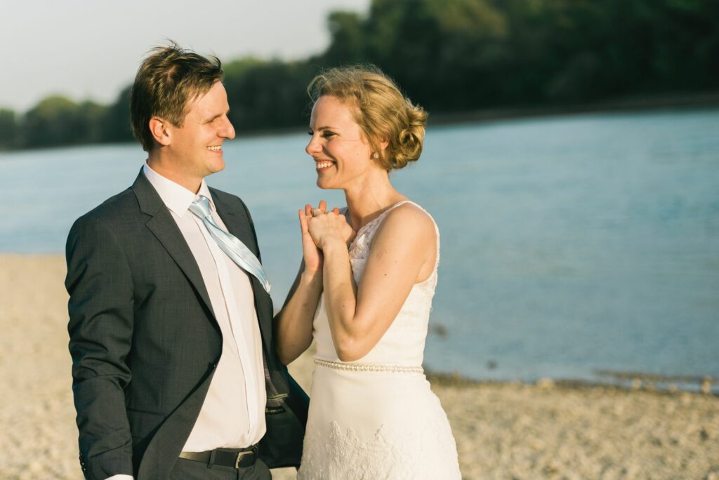 Bride and groom in elegant attire sharing a joyful moment by the riverside on a sunny day.