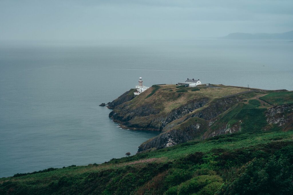Moody aerial view of a coastal cliff with lighthouse and ocean horizon.
