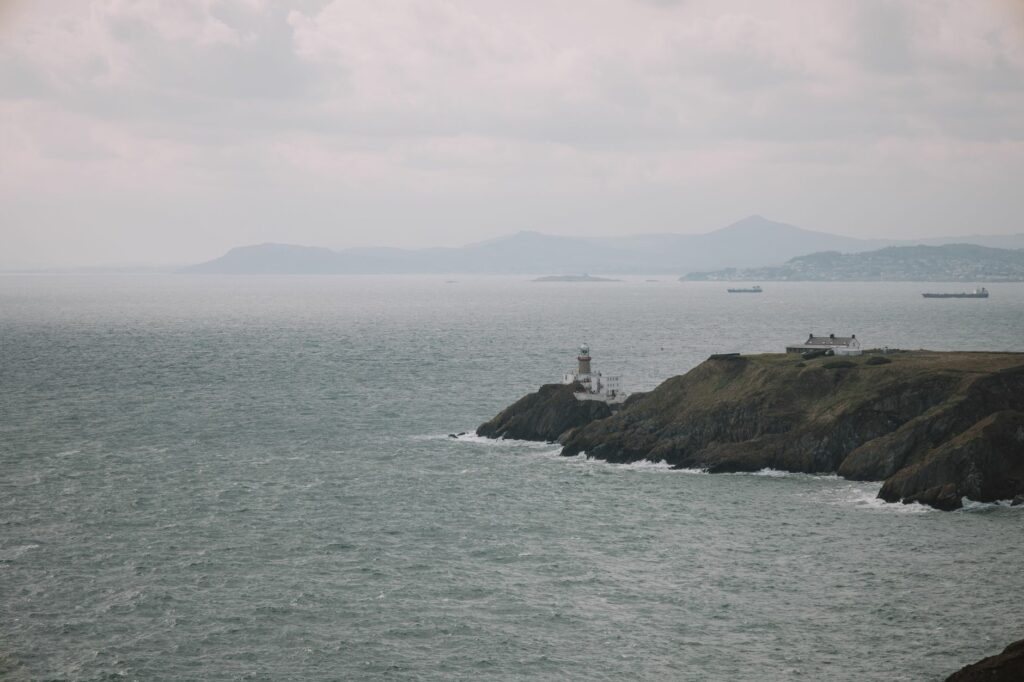 Serene view of Dublin's Baily Lighthouse amidst fog and gentle waves, capturing Ireland's rugged coastline.
