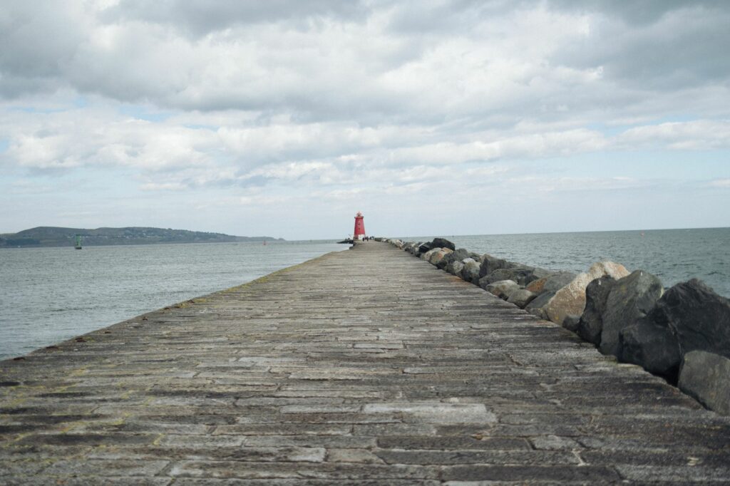 Scenic view of Poolbeg Lighthouse along the stone pier extending into the sea under cloudy skies.
