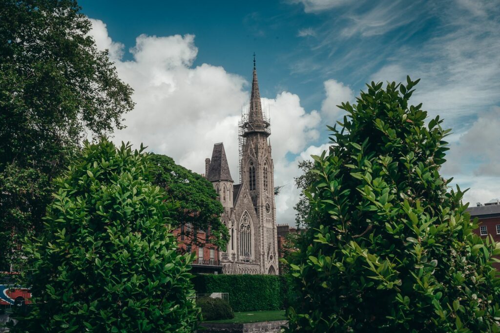 Gothic revival church spire framed by lush greenery under a cloudy Dublin sky.