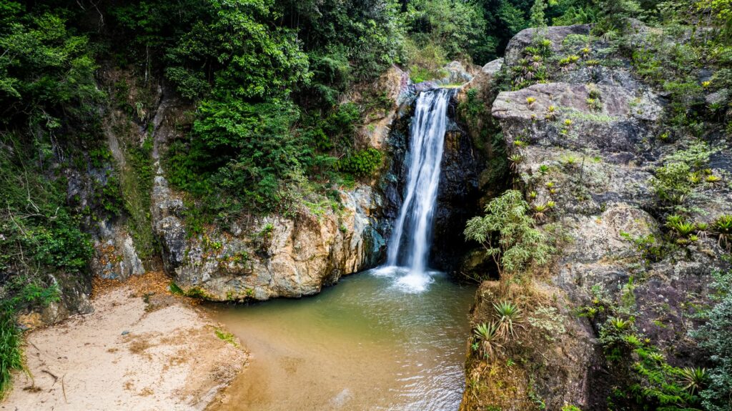 A breathtaking waterfall cascades into a serene pool, surrounded by lush greenery in Jarabacoa, Dominican Republic.
