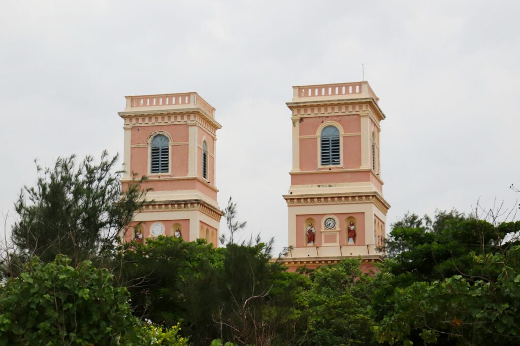 Twin towers of the Eglise de Notre Dame des Anges in Pondicherry, framed by lush greenery.