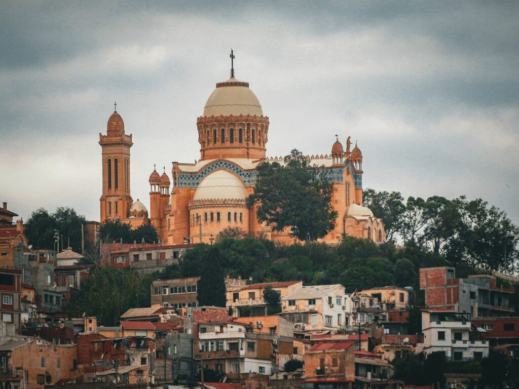 A striking view of the Saint Augustine Basilica in Algiers amidst a dense residential area under cloudy skies.