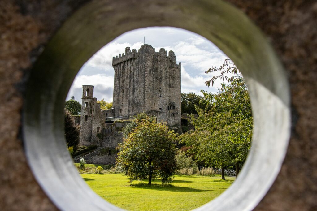 View of Blarney Castle in County Cork, Ireland, framed by a stone arch, under sunny skies.