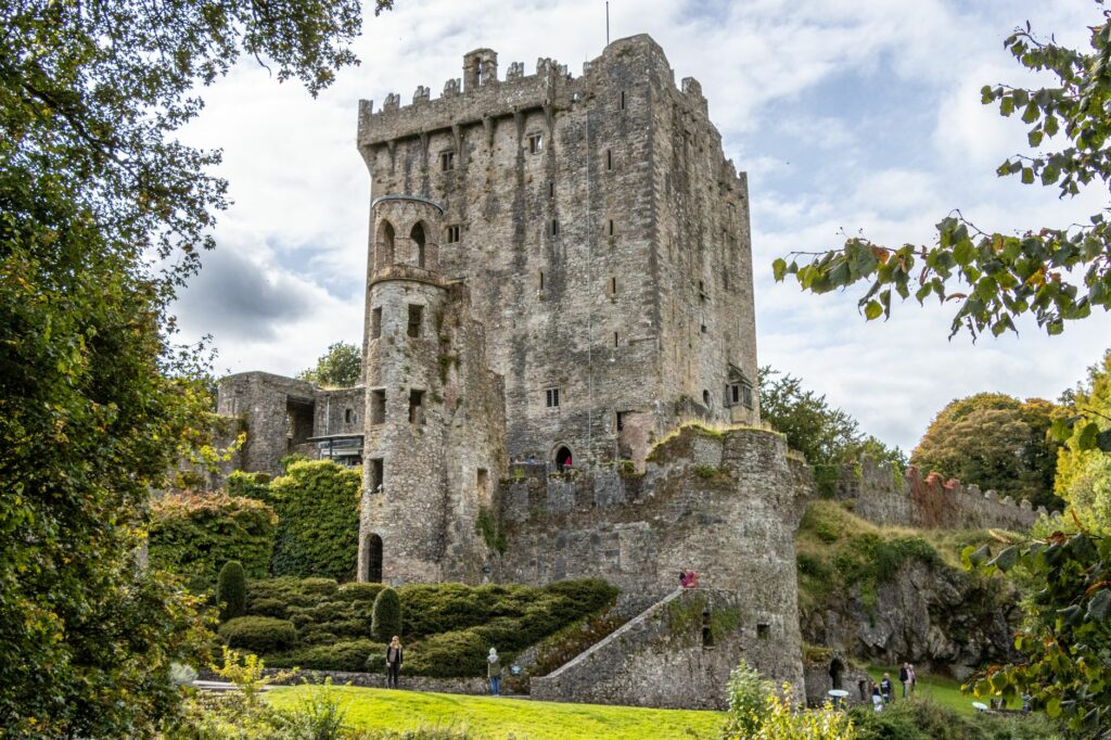 Historic Blarney Castle set against a backdrop of vibrant greenery and a partly cloudy sky.