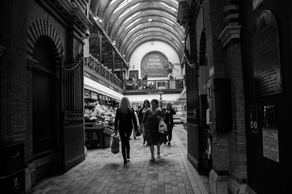 Monochrome view of people walking through Cork's indoor market, highlighting its architectural charm.