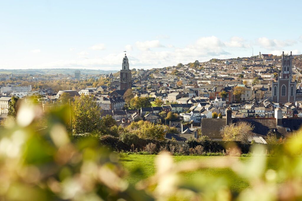 Beautiful view of Cork city with iconic churches and lush greenery, under a bright blue sky.