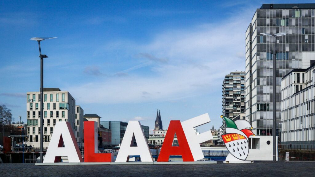 Colorful Alaaf sign with Cologne's cityscape, highlighting its vibrant carnival tradition.