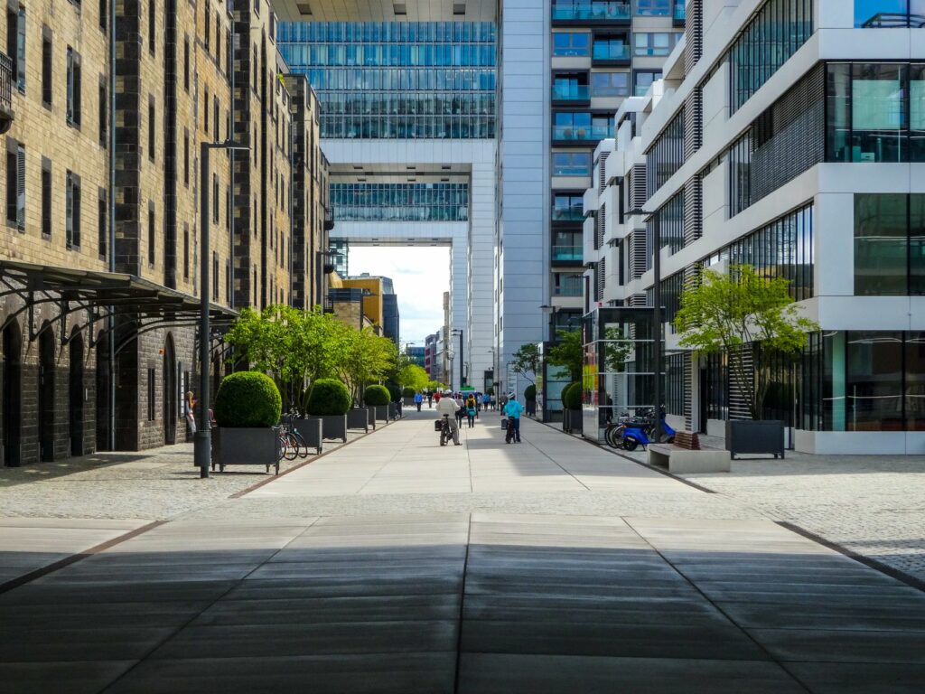 View of a modern city street in Cologne, Germany with pedestrians, trees, and architectural buildings.