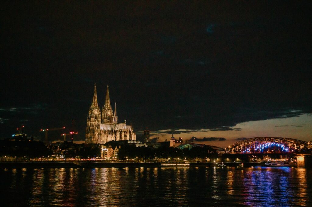 View of Cologne Cathedral and Hohenzollern Bridge illuminated at night, reflecting in the Rhine River