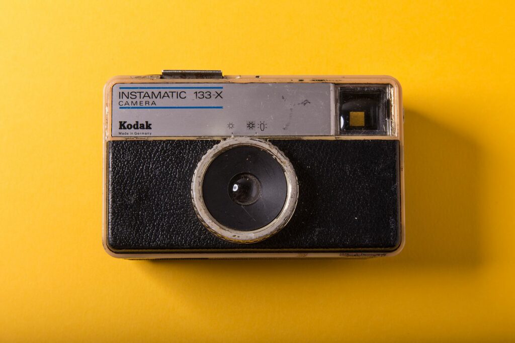 Close-up of a Kodak Instamatic 133-X camera on a bright yellow background enhancing its retro charm.