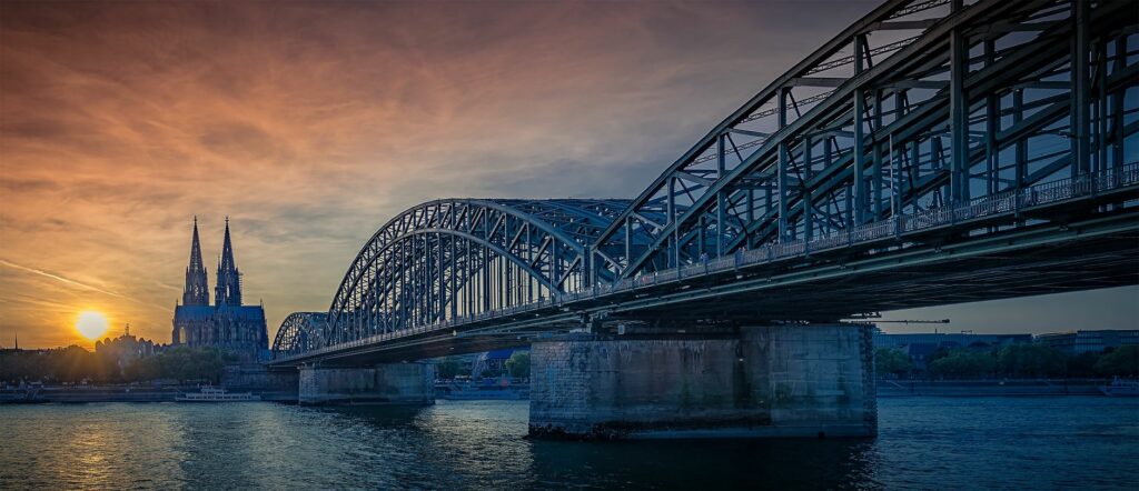 Hohenzollern Bridge and Cologne Cathedral at sunset over the Rhine River.