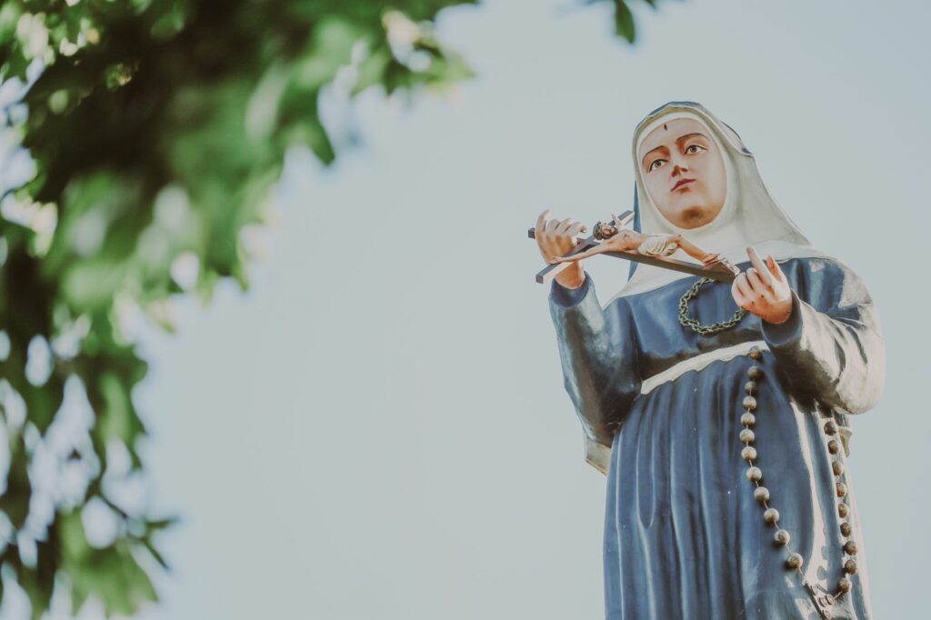 Low angle view of a Virgin Mary statue against a clear blue sky, symbolizing spirituality.