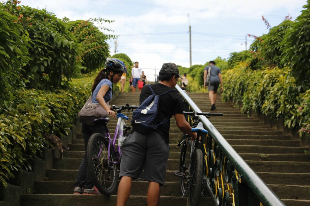 Two cyclists navigate concrete stairs in a green park setting, symbolizing teamwork and outdoor adventure.