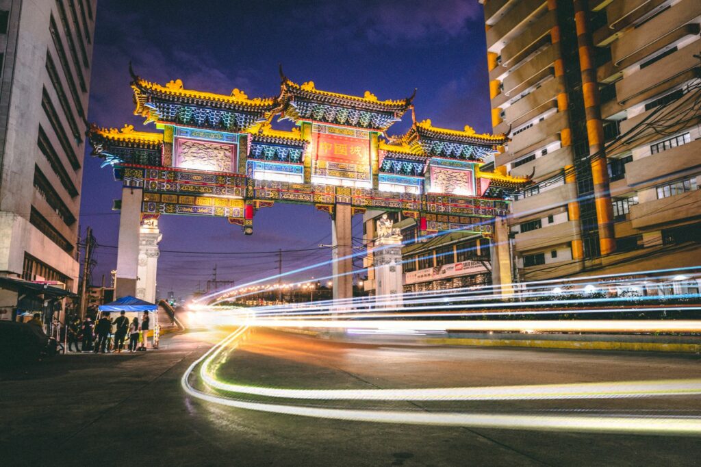 A vibrant night scene capturing the illuminated Chinese gate in Manila, showcasing cultural architecture and city life.