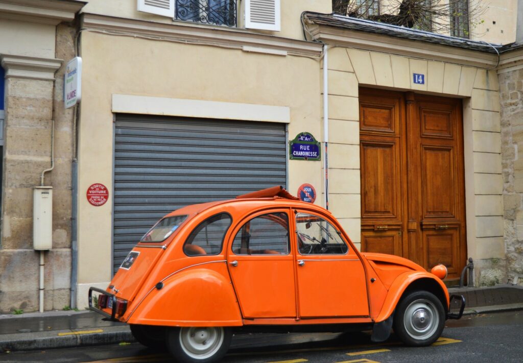 Classic orange car parked on Rue Chanoinesse in Paris, capturing vintage urban charm.