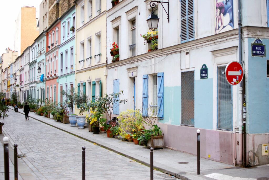 A picturesque street in Paris, featuring pastel-colored buildings and vibrant potted plants.