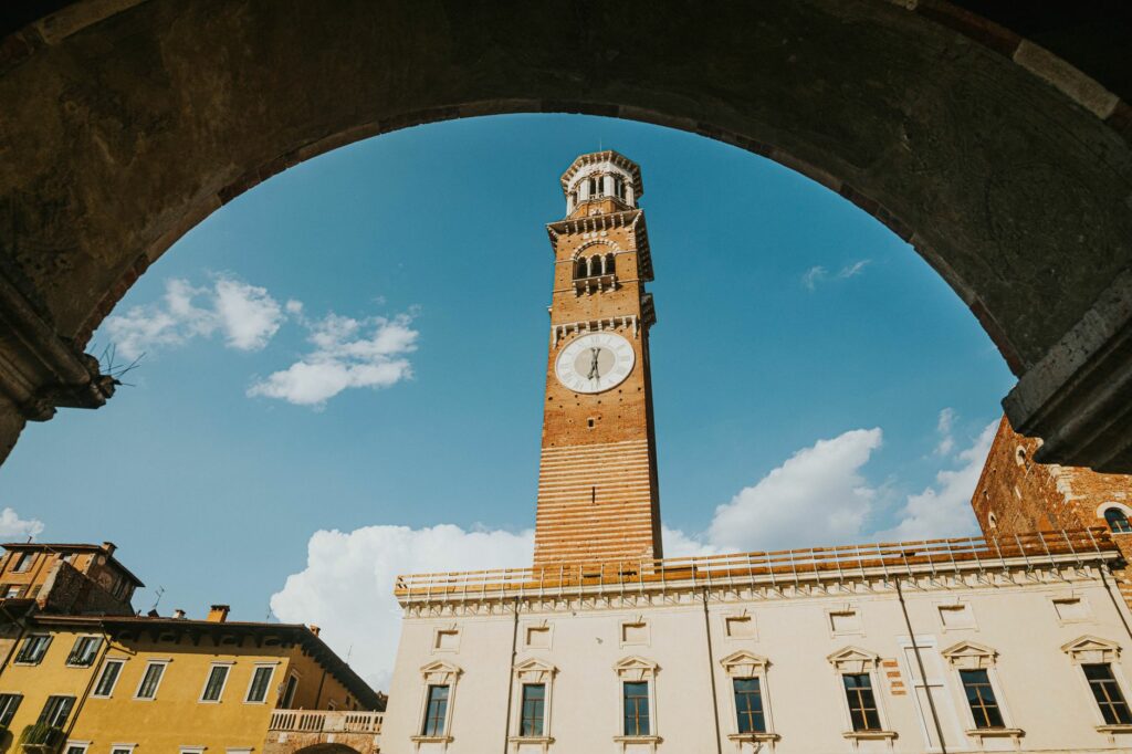 View of Lamberti Tower through archway in Verona, Italy with clear blue skies.