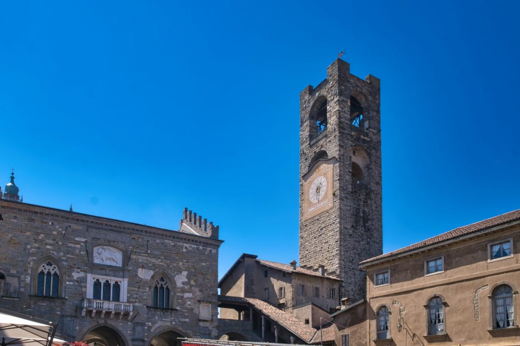 View of the historical Torre Civica and medieval architecture in Bergamo, Lombardy, under a clear blue sky.