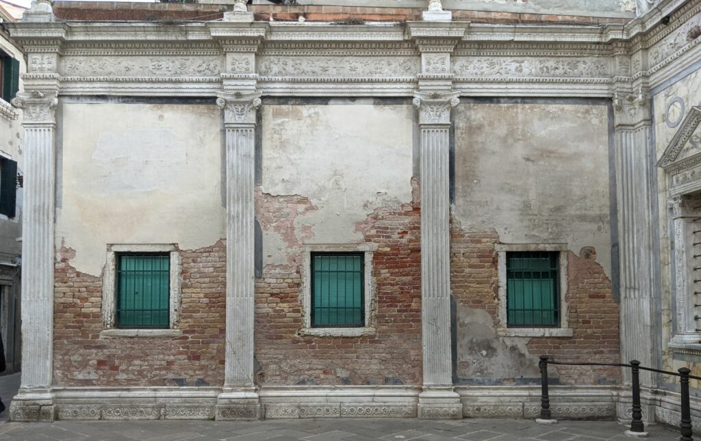 Aged brick and stucco facade with classical columns in Venice, Italy, showcasing rustic charm and historical architecture.