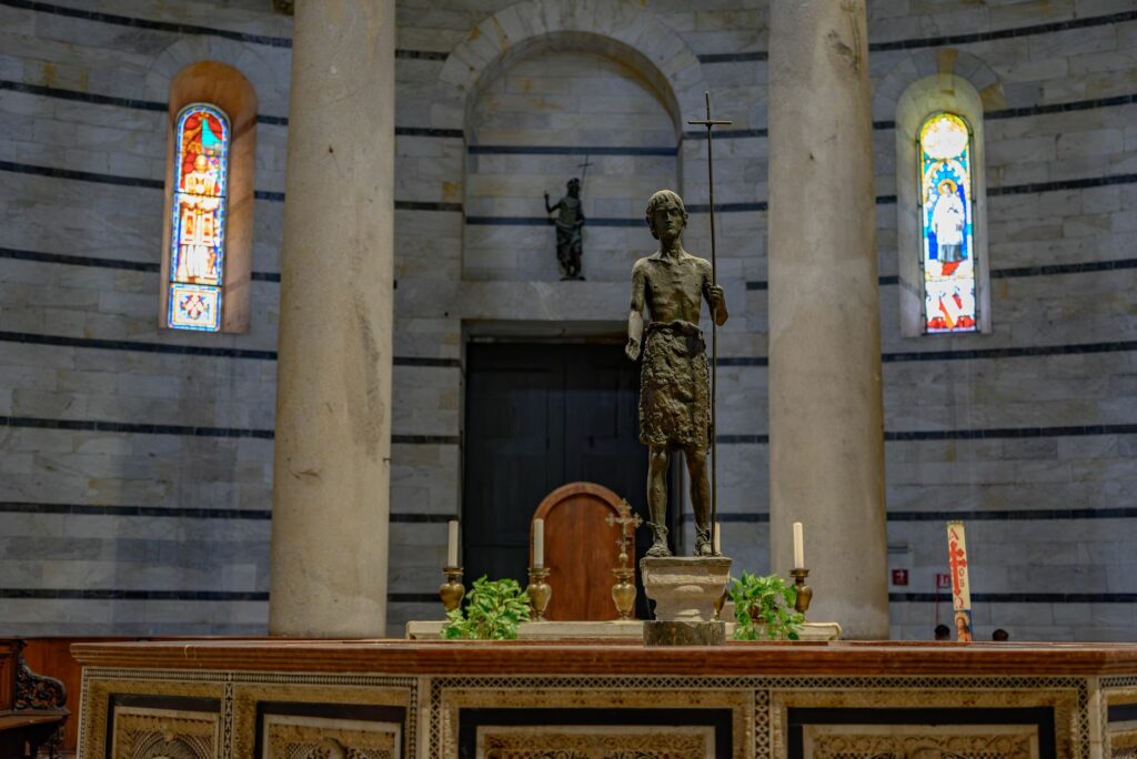 A detailed view of the Pisa Cathedral Baptistery interior featuring a religious statue and stained glass windows.