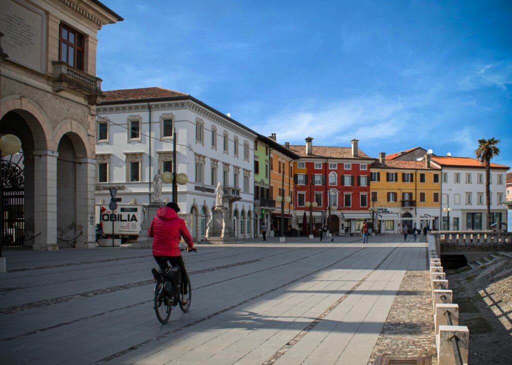 Colorful buildings line a street in Palmanova, Italy, with a cyclist in view.