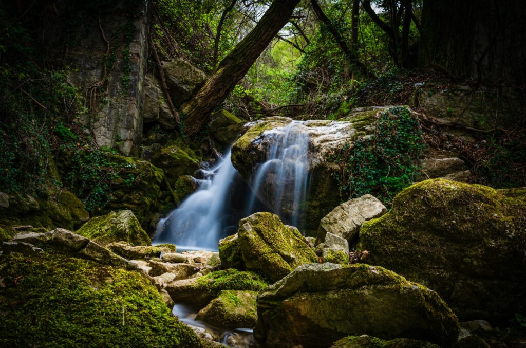 Peaceful waterfall cascading over mossy rocks in a lush Italian forest setting.