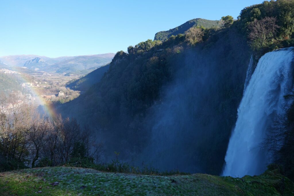 Breathtaking view of Marmore Falls in Umbria, Italy with a vibrant rainbow and lush landscape.