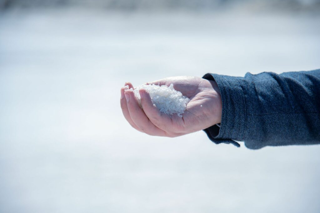 A close-up view of a hand holding white salt crystals outdoors, capturing texture and detail.