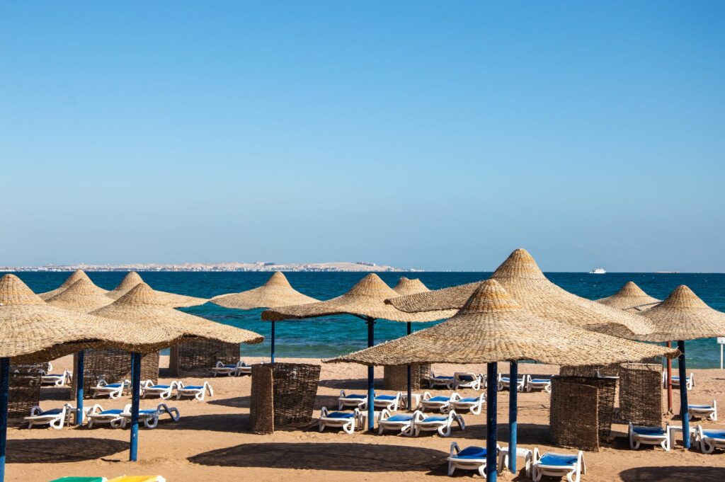 Wide view of a beach lined with straw umbrellas, sun loungers, and a calm blue sea.