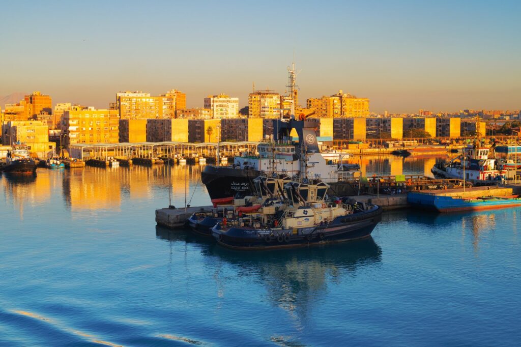 Sunlit view of a bustling harbor in Suez, Egypt showcasing boats and cityscape.