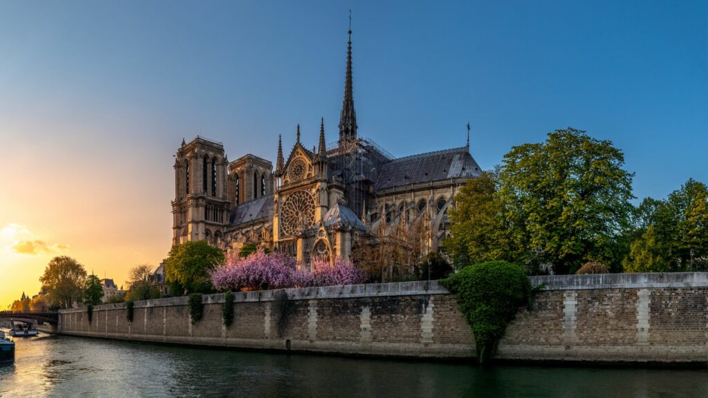 Notre Dame Cathedral bathed in warm sunset light with river view.